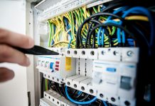 בטיחות בעבודות חשמל בשיפוץ הבית Hand of electrician working on a circuit breaker panel with colorful wires, ensuring safe electrical connections.